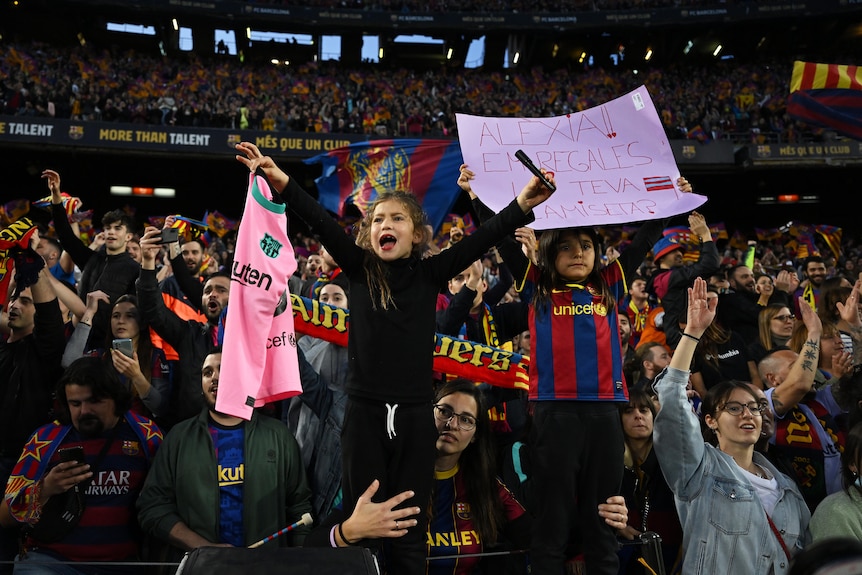 Deux jeunes filles sont tenues en l'air dans la tribune, alors qu'elles encouragent leurs équipes féminines de football lors d'un match. 