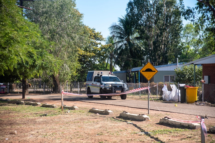 A police car parked at the front of a house on the street of a remote community sectioned off with crime tape.