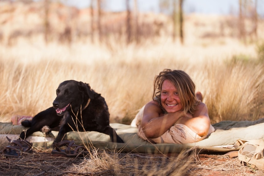 From the film Tracks a young tanned and dirty woman lies in a makeshift camp next to a dog