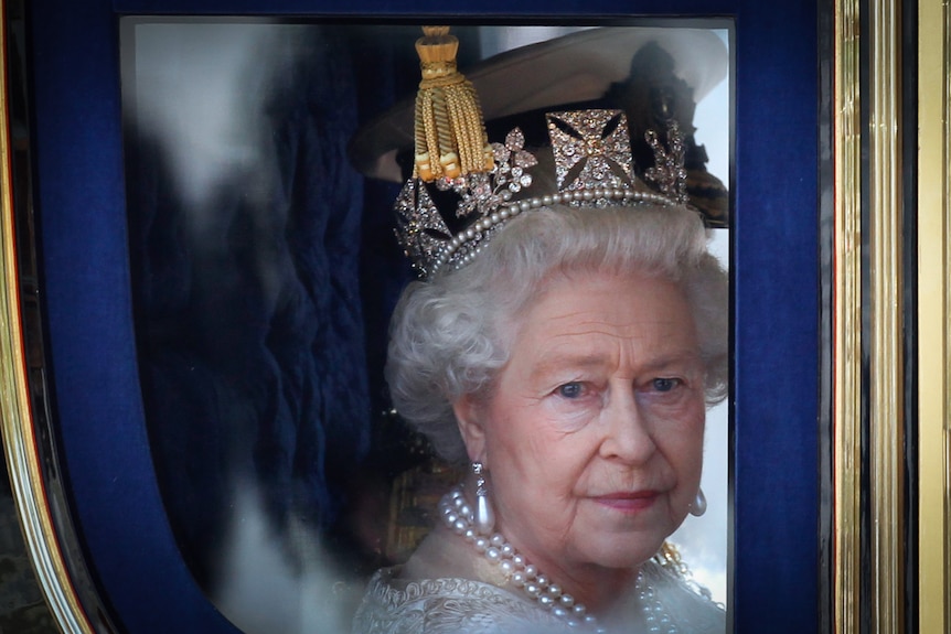 A close up of Queen Elizabeth wearing a crown staring out of the window of her carriage.