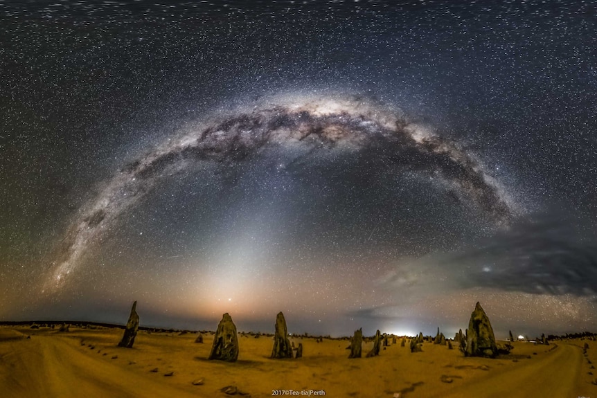 A number of large termite mounds jut out of a dusty landscape, with the starry night sky glowing above.