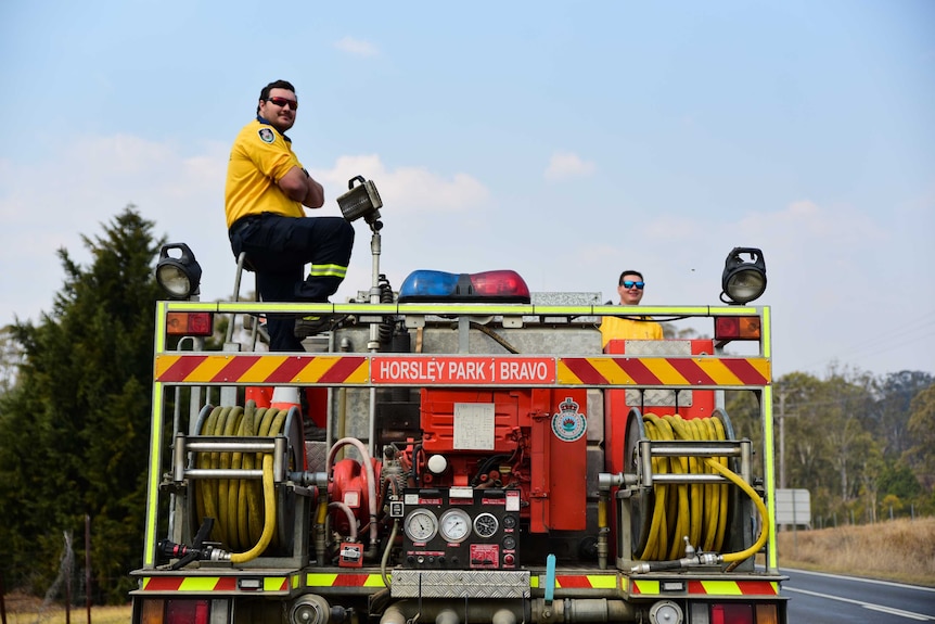 A man stands on top of a fire engine, he is wearing a RFS polo-shirt and sunglasses.