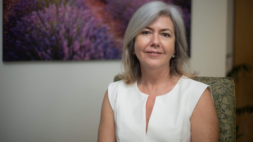 Woman with silver hair stands in front of a purple painting