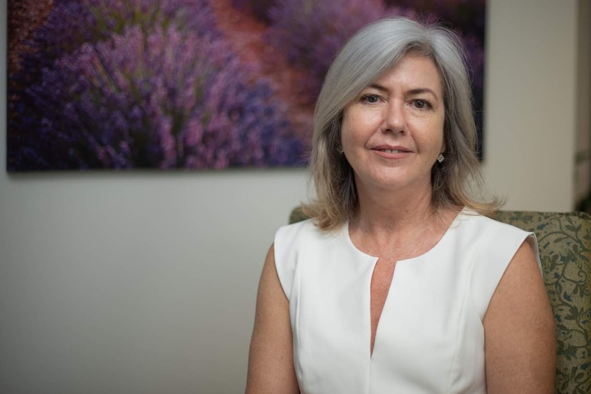 Woman with silver hair stands in front of a purple painting