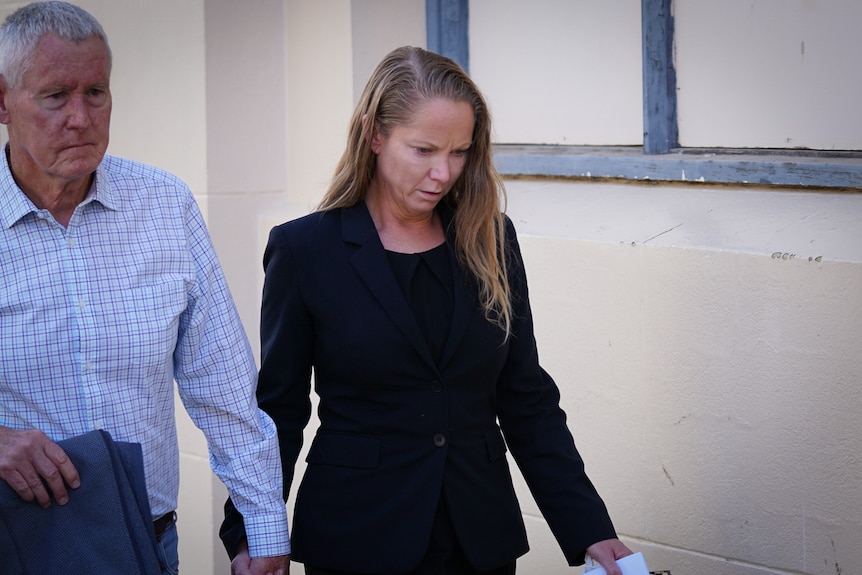 A woman in dark clothing walks along holding the hand of an older man.