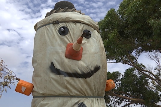 A giant 'snowman' made from a white tarpaulin draped over tyres and hay bales, with a traffic cone nose.