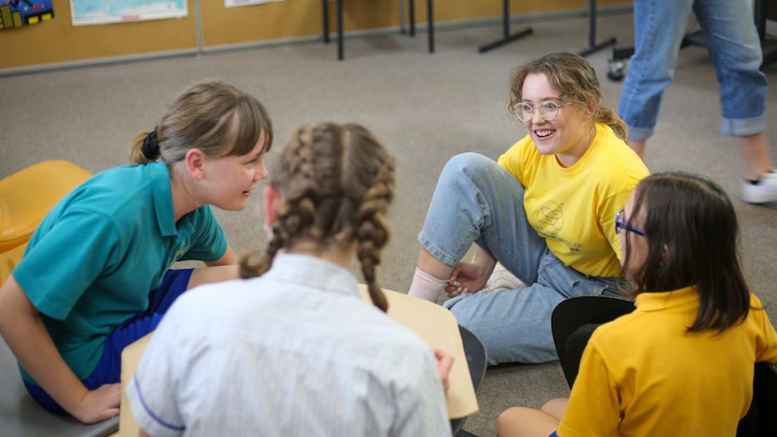 Women smile at two girls, sitting down in a classroom