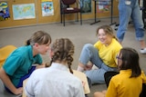 Women smile at two girls, sitting down in a classroom