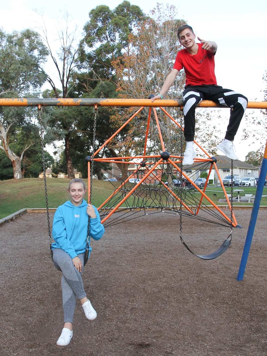 Two youths hang off a playground swing set