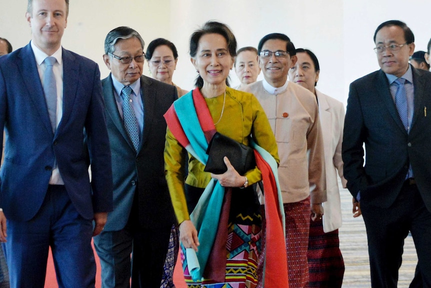 Aung San Suu Kyi surrounded by men walking through an airport