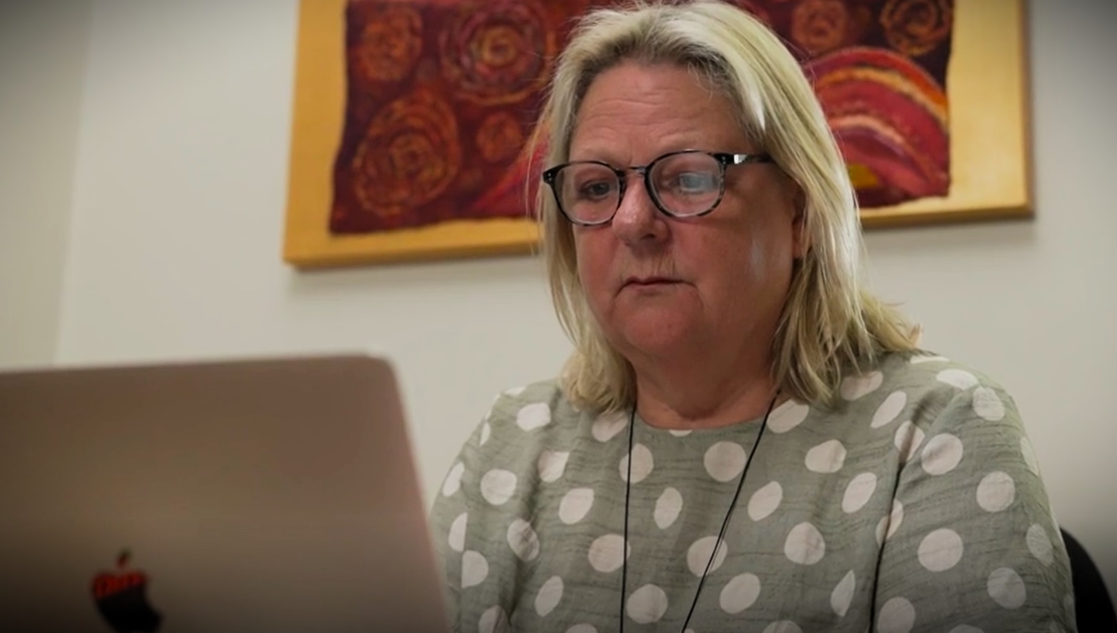 За ноутбуком сидит блондинка средних лет в очках.