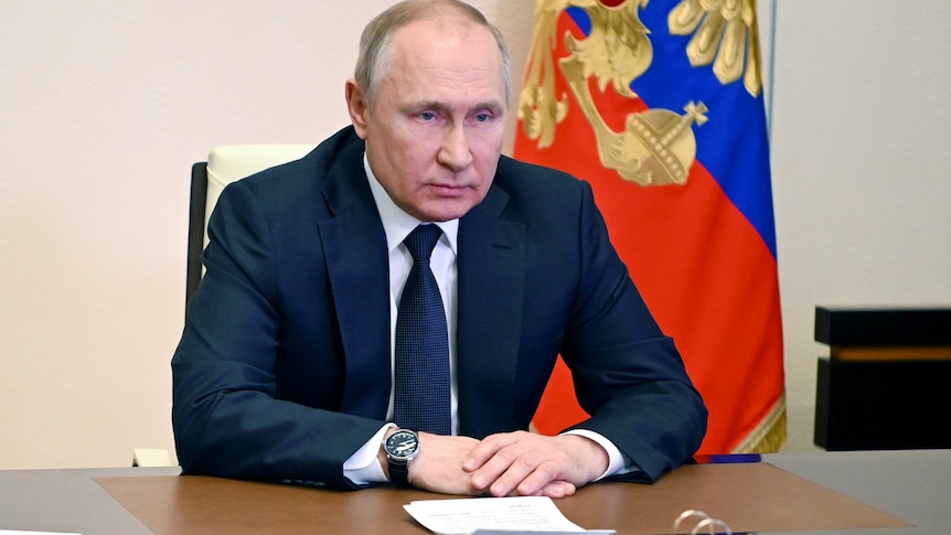 Russian President Vladimir Putin stares in front of him with an angry look from behind a desk.