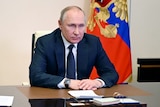 Russian President Vladimir Putin stares in front of him with an angry look from behind a desk.