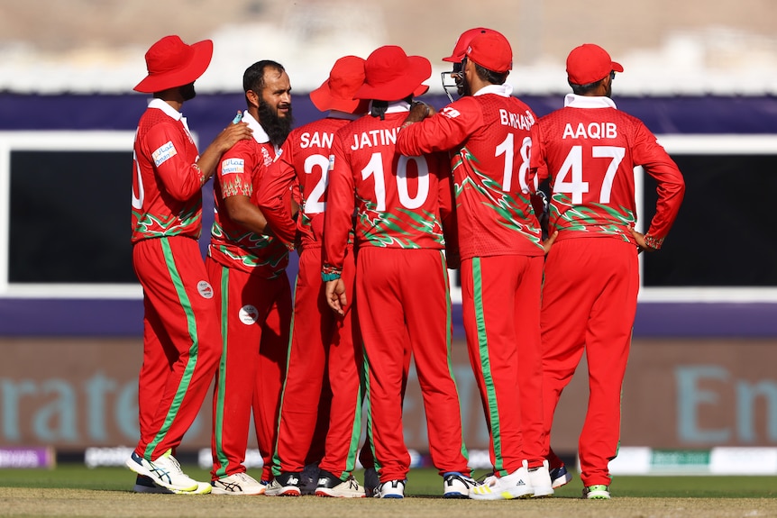 A group of Oman cricketers crowd around a bowler to congratulate him on taking a wicket in a T20 World Cup game.