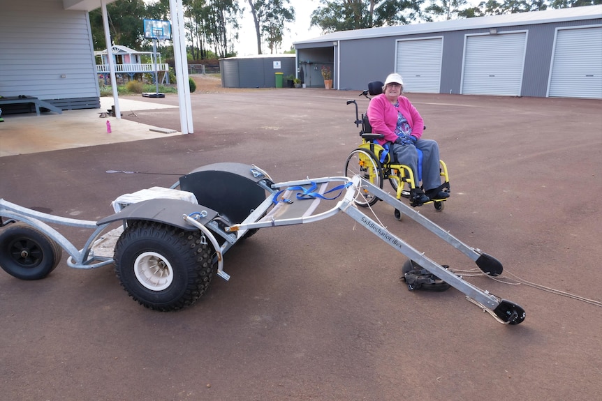 A woman in wheelchair stand next to a carriage on the ground. 