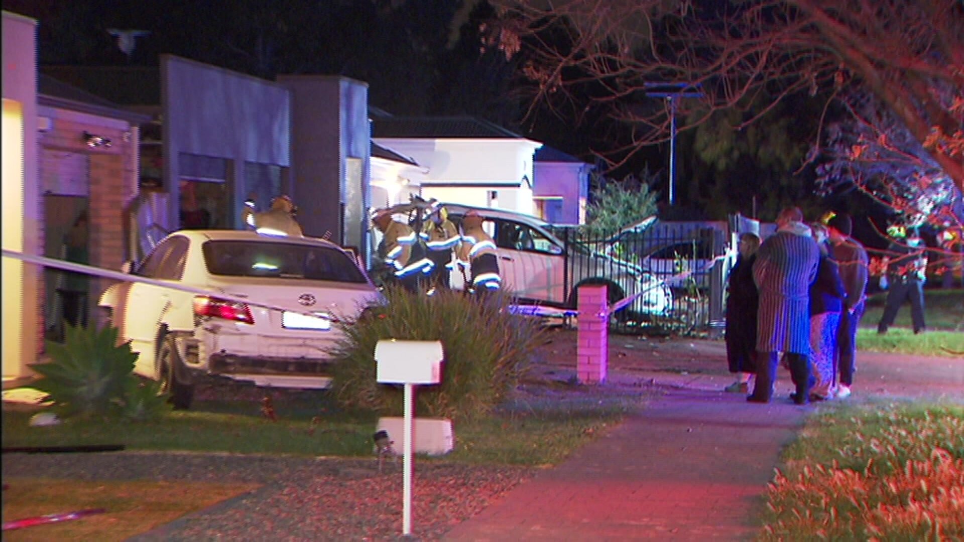 A damaged limousine in front of a house and a four wheel drive and people watching at night