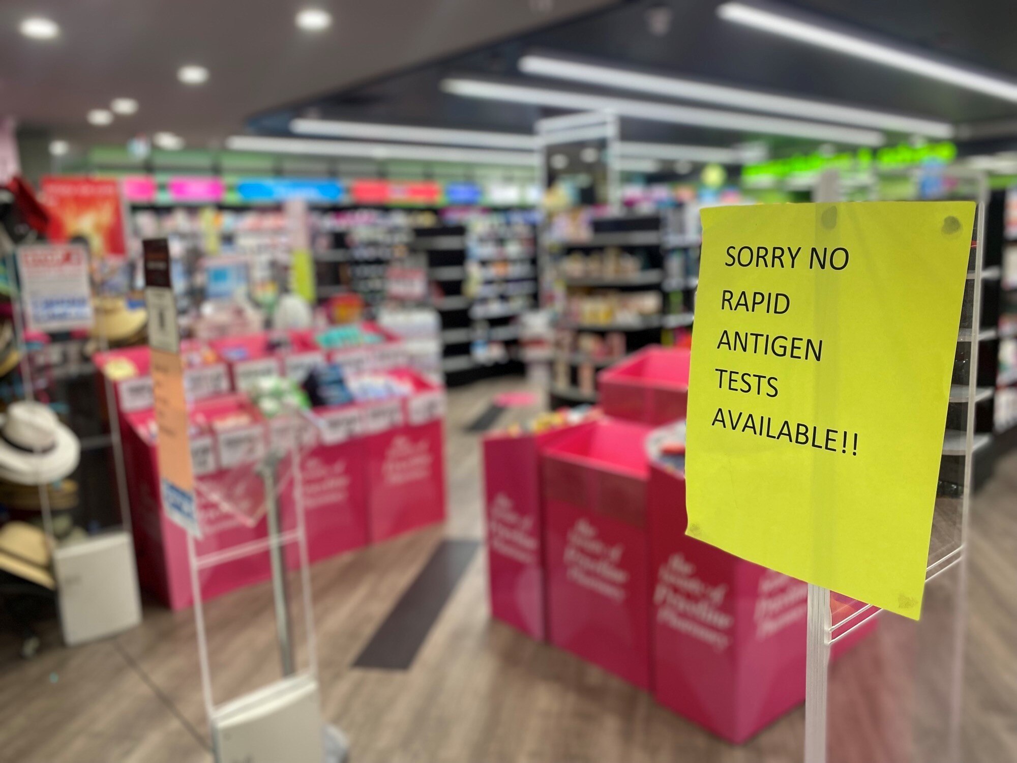 A fluro yellow sign at the entry to a chemist reads "sorry no rapid antigen tests available!!"