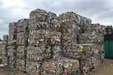 Big, squared bales of waste to be recycled, stacked up in a yard.