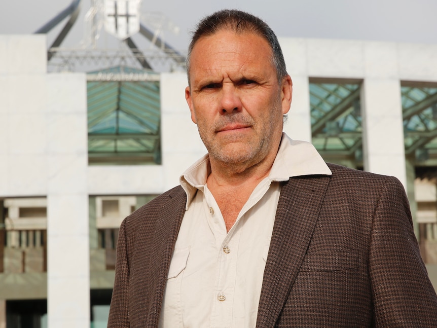 a man stands in a blazer wearing a white shirt