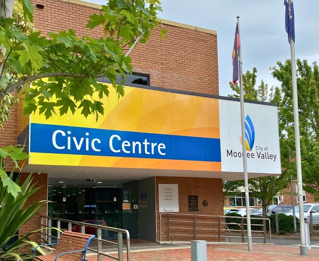 Two flags hang limply from poles outside a brick building that says "civic centre" and "moonee Valley"