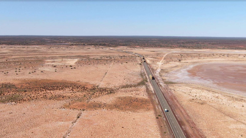 An aerial shot of drought-stricken land in Meekatharra, with trucks driving on the highway.