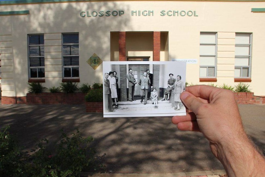 A black and white photo is held in front of a cream building that says Glossop High School.