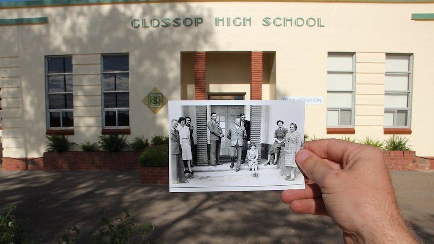 A black and white photo is held in front of a cream building that says Glossop High School.