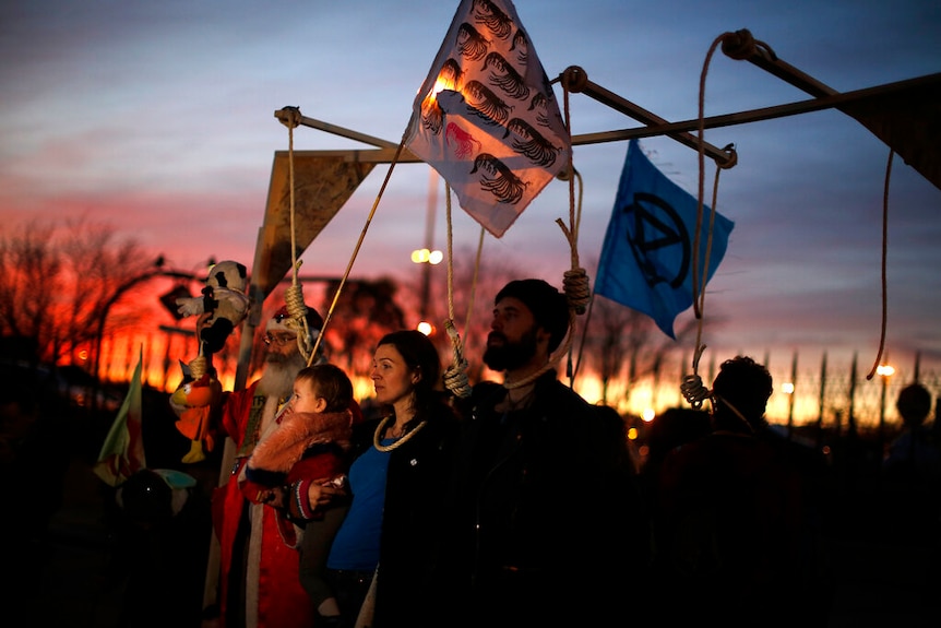 Activists stand under loose nooses attached to a frame at dusk outside the COP25 conference in Madrid.