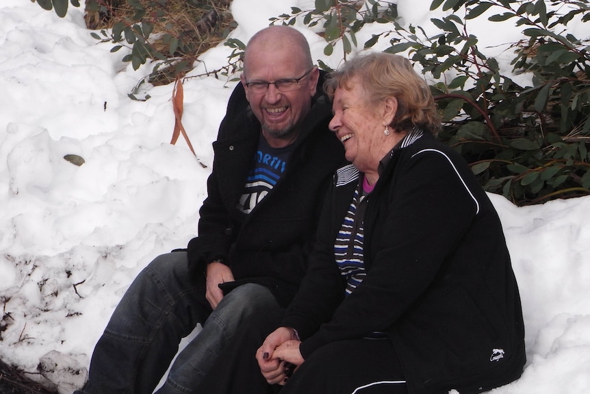 A man and woman sit smiling on a snow bank.