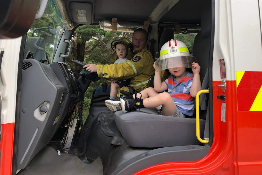 A woman and two children sit inside a fire truck