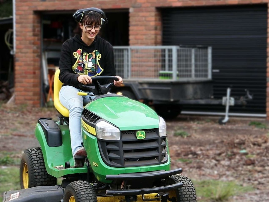 A teenage girl smiles while using the ride-on mower