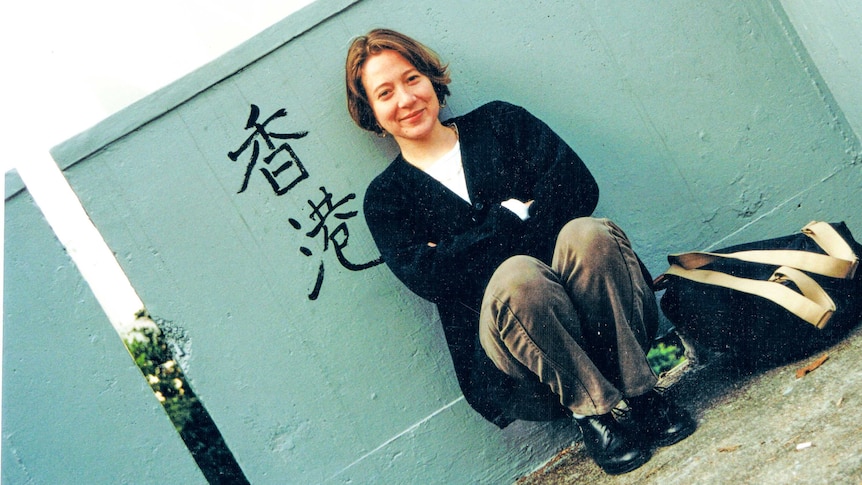 A woman sits next to a green wall with the Chinese characters for Hong Kong painted on it.