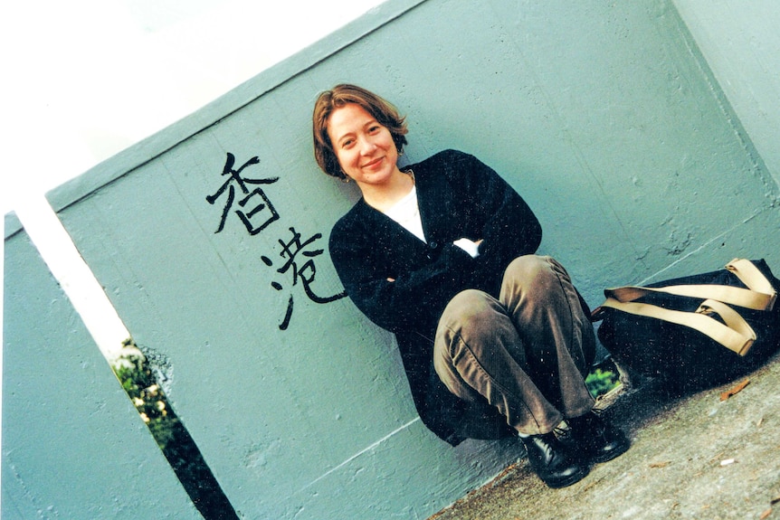 A woman sits next to a green wall with the Chinese characters for Hong Kong painted on it.