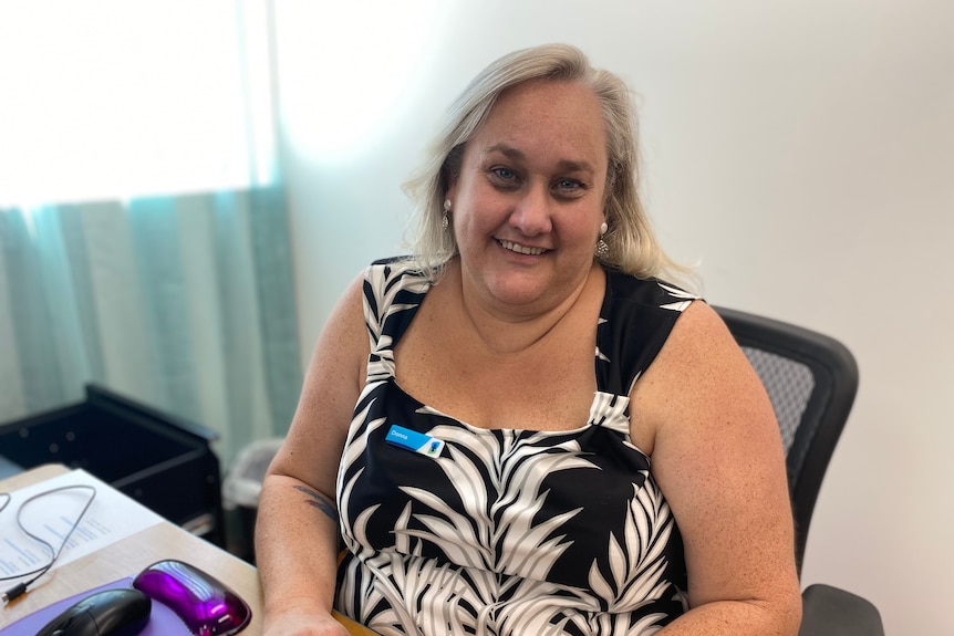 A woman, wearing a badge, sits smiling at her desk