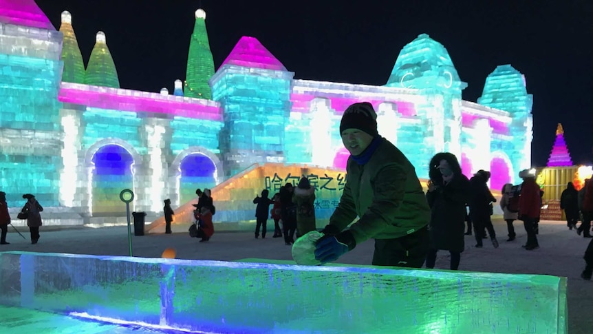 A man plays ping pong on an ice table, with a colourful structure built from ice in the background.