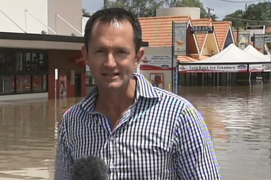 O'Brien looking to camera with flooded street and shops in background.