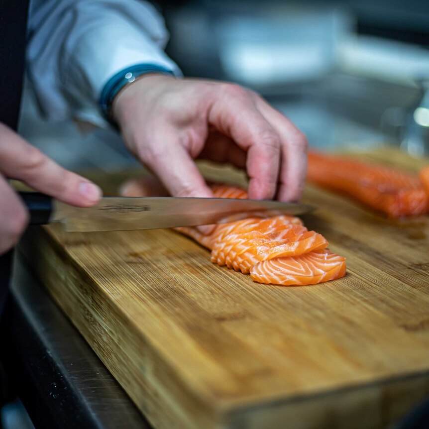 Closeup of hands slicing a raw salmon fillet.