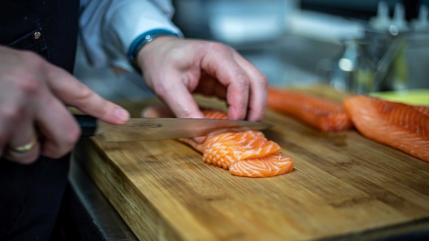 Closeup of hands slicing a raw salmon fillet.