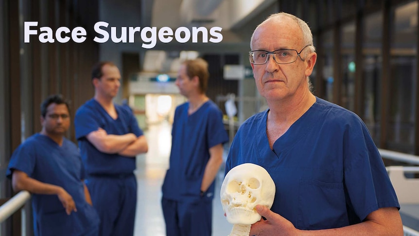 Man in scrubs holding a model skull with a spine attached, other health people in scrubs seen in the back