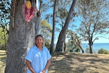 A woman in a light blue shirt stands in front of a tree with an Indigenous flag painted into a knot