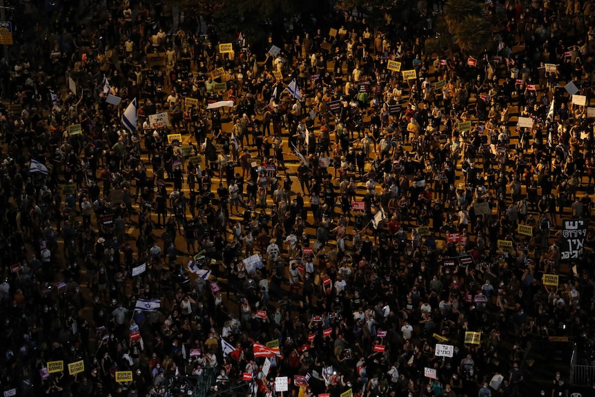 A crowd of protesters hold signs during a demonstration against Israel's government in a square