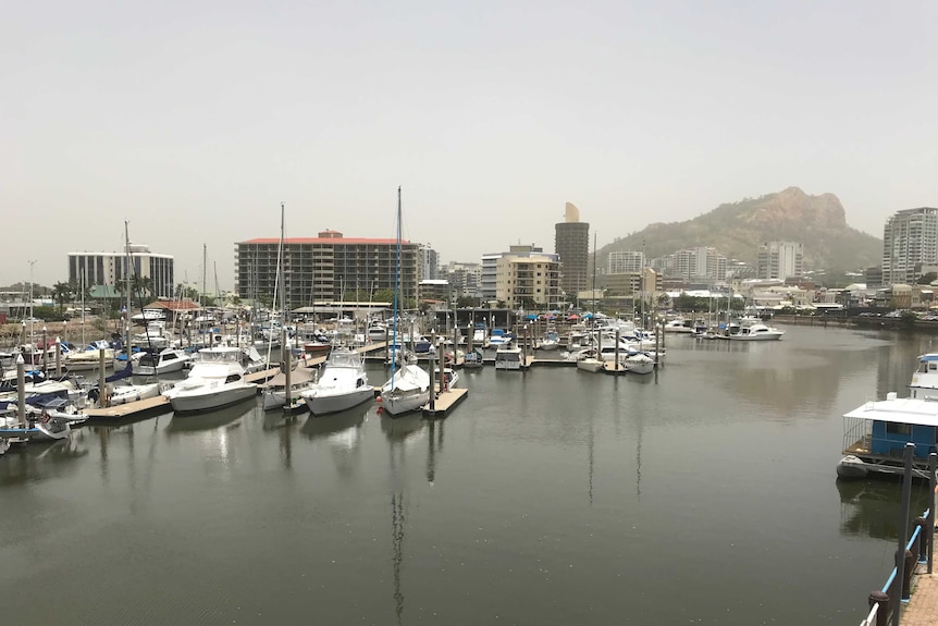 On an overcast day a marine is full of boats and yachts. Hotels, apartment blocks and a rocky mountain are in the background