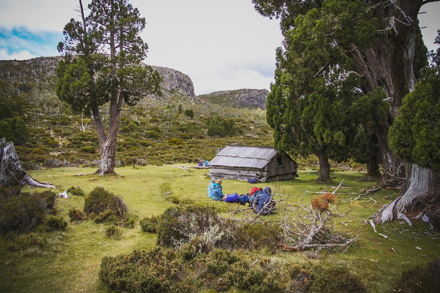 A group of people sit in a campground near a rustic shack.