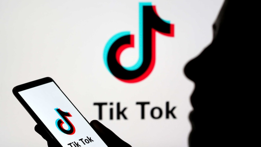 A picture of the tiktok logo, which looks like a musical note, with a silhouette of a person holding a phone.