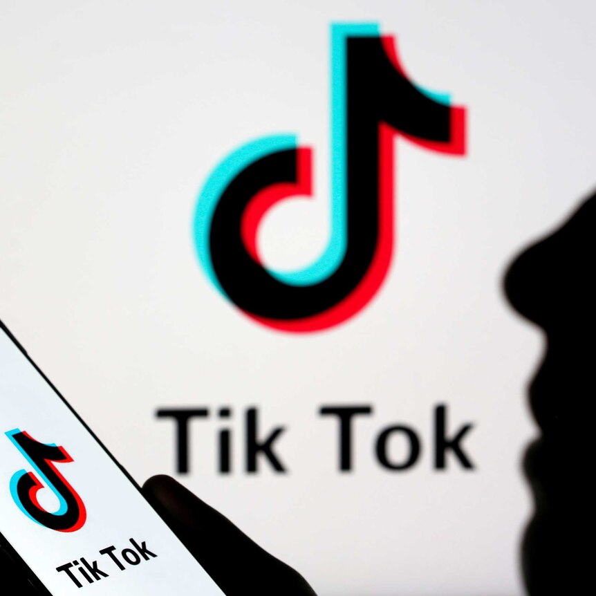 A picture of the tiktok logo, which looks like a musical note, with a silhouette of a person holding a phone.