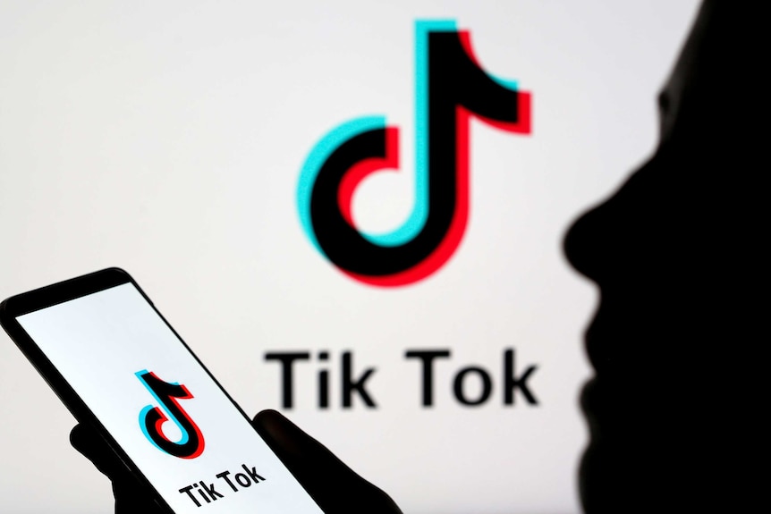 A picture of the tiktok logo, which looks like a musical note, with a silhouette of a person holding a phone.