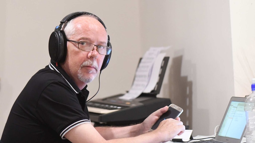 Dan McGarry looks at the camera with headphones on while holding a phone, in front of a laptop.