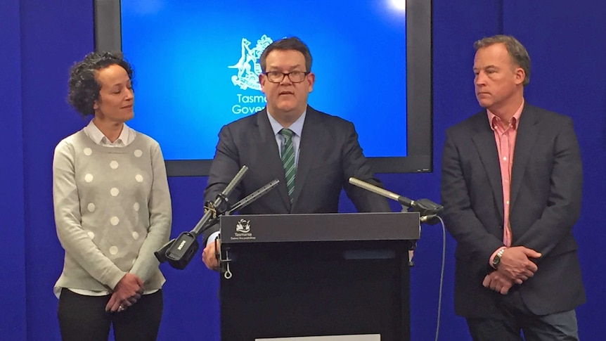 Matthew Groom stands at a podium flanked by his wife, Ruth and Tasmanian Premier Will Hodgman.