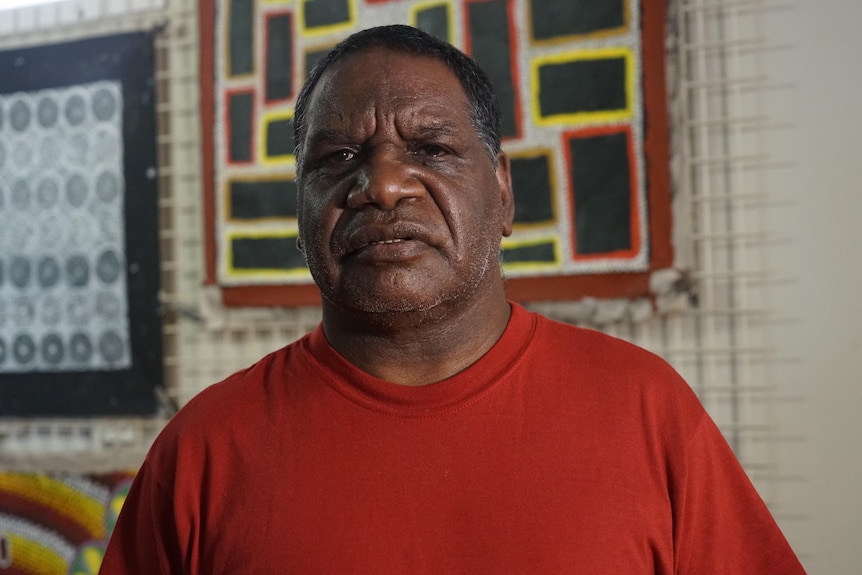 Derek Walker looks at the camera from front on with art on the wall behind him.