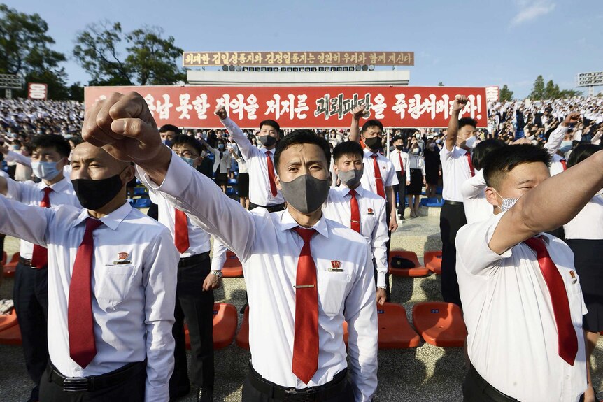 A group of young men in white shirts, red ties and face masks holding their fists up